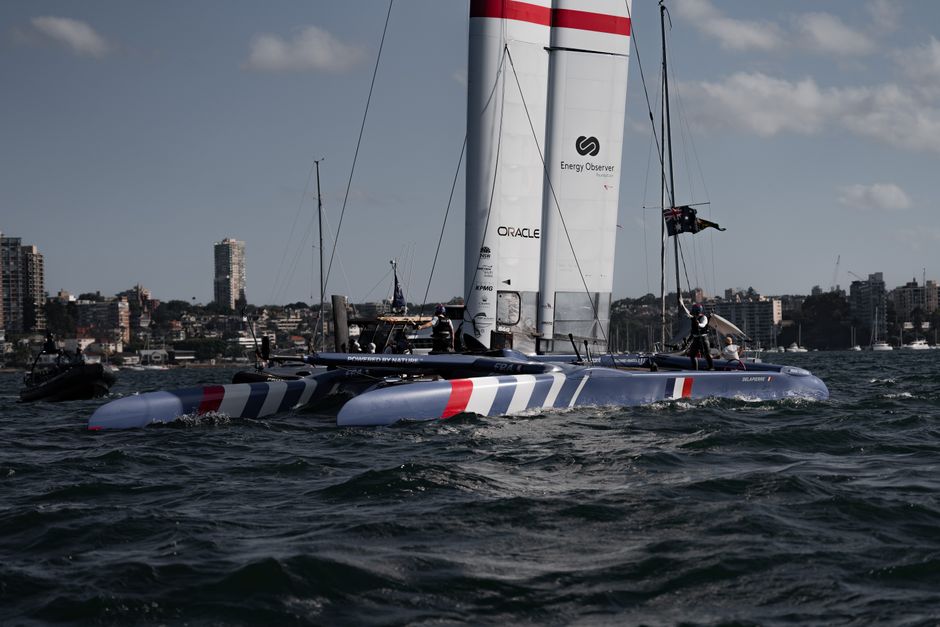 Dynamic scene of an F50 foiling catamaran during a sailing race in Sydney Harbor.